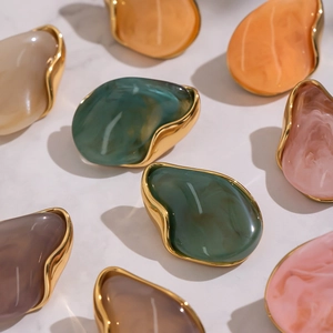 Irregular chunky resin stud earrings with gold metal base on white marble background