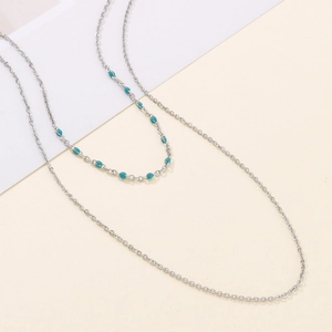 Détail d'un collier double épaisseur en acier inoxydable avec perles turquoise sur chaîne