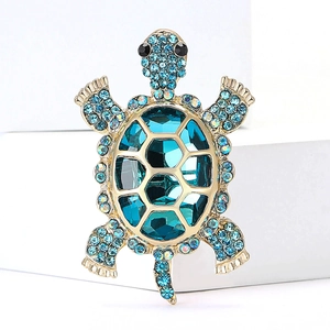 Detailed close-up of a golden turtle brooch with a faceted blue crystal and rhinestones