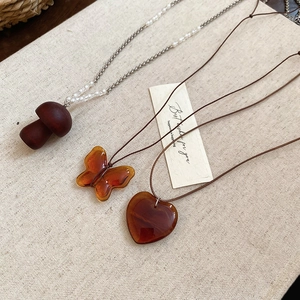 Dettaglio dei ciondoli in resina ambrata a forma di fungo e farfalla su collana di perle