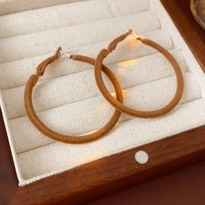 Detailed view of brown flocked hoop earrings on a velvet wooden jewelry display box
