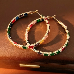 Close-up of gold hoop earrings with multi-colored rectangular zircon stones on leather