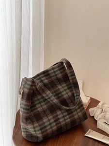 Sac bandoulière en laine à carreaux rétro marron et vert posé sur une table en bois massif