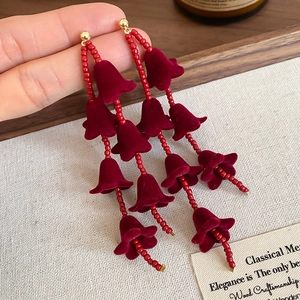 Détail de boucles d'oreilles muguet en flocage rouge tenues devant un fond vintage