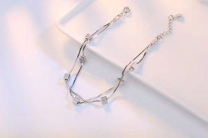 Detail view of silver double snake chain bracelet with polished cube charms and leaf tag