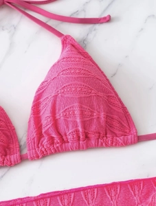 Close-up of rose red bikini top showing textured fabric and triangle cup detail