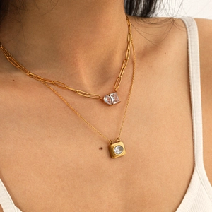 Detail of layered gold paperclip and fine chain necklaces with sparkling zircon pendants