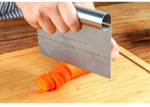 Close-up of stainless steel bench scraper with measurement markings cutting carrots