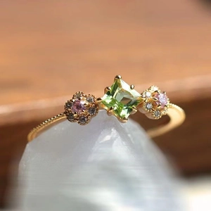 Elegant gold ring with square peridot gem and floral accents on a rustic white stone