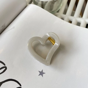 Close-up of heart-shaped grey resin hair claw clip with golden metal spring on white book