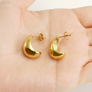 Detailed view of polished 18K gold C-shaped titanium steel earrings held in palm