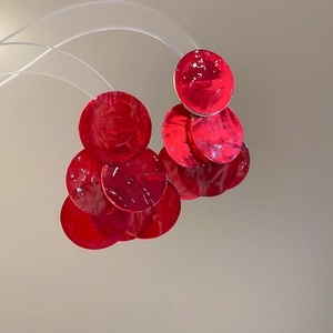 Detailed close-up of red circular shell-like resin discs forming a tiered tassel earring