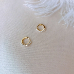 Elegant gold pearl hoop earrings for women on a soft beige background with white feather