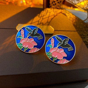 Detailed view of round enamel earring with hummingbird and flower pattern on dark wood
