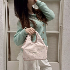 Close-up of pink floral canvas lunch bag with text label held by a hand in natural light