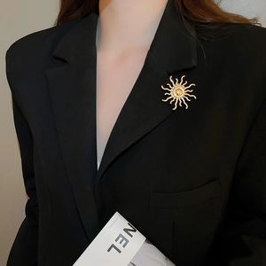 Detailed view of a gold sunburst brooch with pearl on a black blazer lapel