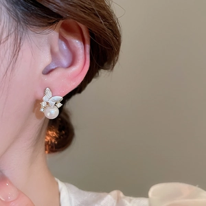Close-up of butterfly pearl drop earrings with sparkling rhinestones worn on a model