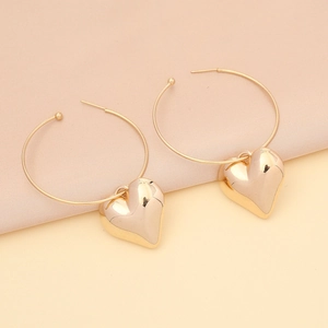 Close-up of golden heart earrings with polished finish on a soft fabric background