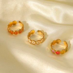 Detailed macro of daisy enamel rings in white and orange on creamy silk fabric background