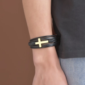 Détail d'un bracelet multicouche pour homme en cuir noir avec une croix en métal doré