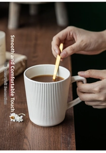 Close-up of white relief ceramic mug with vertical stripes and golden spoon on wood table