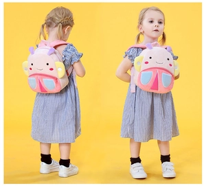 Pink cartoon plush backpack for kids with colorful wings shown in use by a child