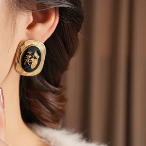 Vintage oval black enamel earrings with gold horse carriage relief on model