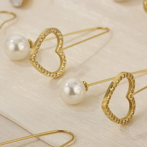 Macro detail of gold heart-shaped earring with white pearl and sparkling rhinestones