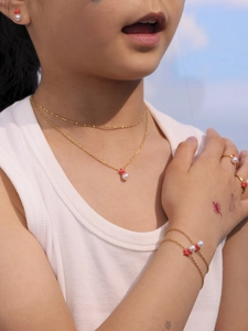 Detalle de set de joyas doradas con flores rojas y perlas para niña al aire libre