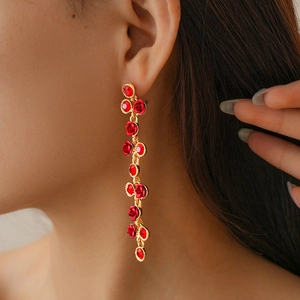 Détail d'une boucle d'oreille dorée à pompon avec roses rouges et cristaux sur un mannequin