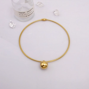 Détail d'un pendentif sphère dorée minimaliste sur une fine chaîne serpent élégante