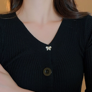 Detail of a black V-neck ribbed knit top with a delicate butterfly charm and button