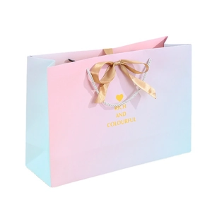 Pink and blue gradient paper gift bag with white handles and a golden satin ribbon bow