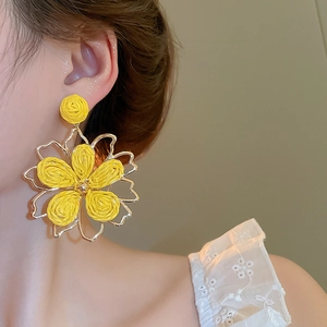 Detailed close-up of yellow woven flower earrings with gold metal petals on a model