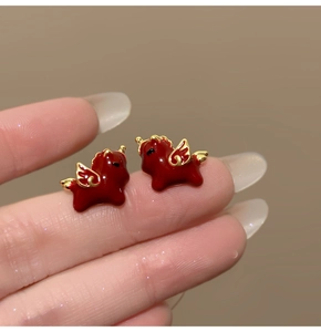 Detailed close-up of 18k gold plated red enamel pony stud earrings on finger tip