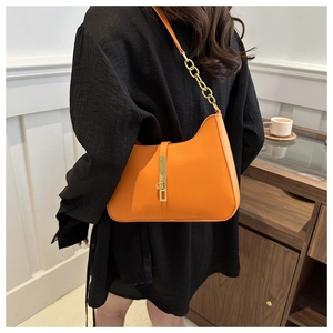 Detail of bright orange hobo bag featuring a bold gold chain strap and stylish buckle closure