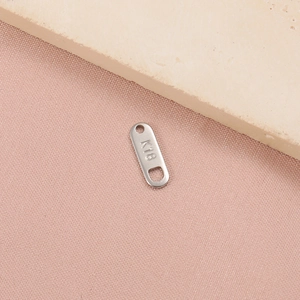 Macro shot of silver stainless steel oval K18 jewelry connector tag on pink fabric
