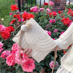 Borsa a tracolla in paglia intrecciata bianca con ciondoli pompon in un giardino di rose