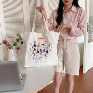 Detailed view of colorful floral embroidery on high-capacity white canvas tote bag