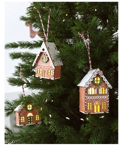 Three glowing wooden gingerbread house ornaments hanging on a green Christmas tree