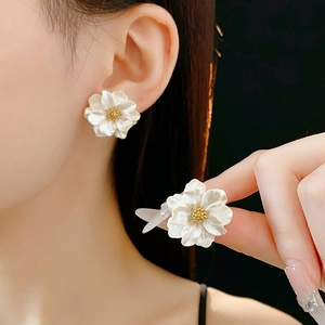 Detailed view of 3D white flower resin earrings with golden stamens worn by a model