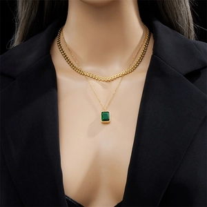 Layered gold necklace with emerald-cut green gemstone pendant worn by a model