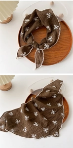 Detailed view of dark brown scarf featuring white floral embroidery and crochet lace edges