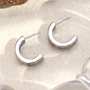 Détail de boucles d'oreilles argentées en C avec torsade dorée sur surface en pierre