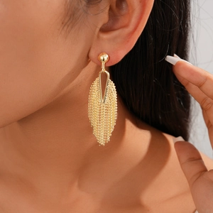Close-up of golden geometric tassel earrings worn by a model on a white background