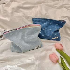 Close-up of denim cosmetic bags with bow texture and pink zipper detail in soft lighting