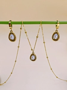 Detailed close-up of golden necklace and earrings set featuring white oval pearls