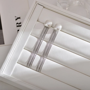 Close-up of elegant long tassel pearl earrings with silver metal fringe on a white display box