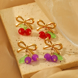 Detail of gold bowknot stud earrings with red and purple cherry-shaped beads on stone