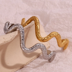 Macro detail of hammered texture on wavy snake-shaped bangles in gold and silver finish
